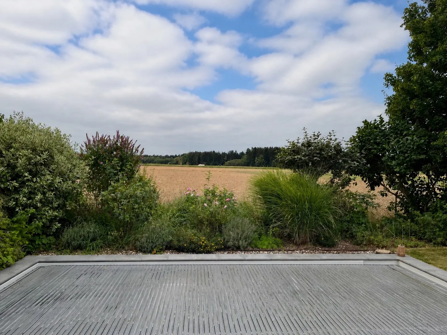 Terrasse mit Blick über ein abgeerntetes Feld, davor ein bewachsenes Staudenbeet